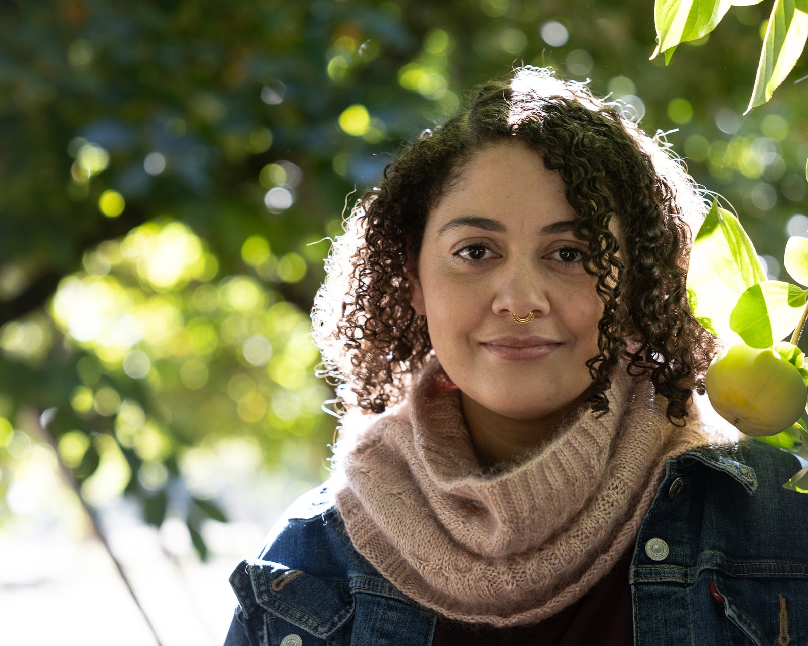 Woman wearing a pink scarf and denim jacket standing in front of green foliage